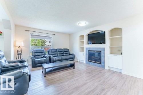 Living room featuring wood-finish flooring, a fireplace with blue tile surround, and integrated shelving with lower cabinetry - 3525 22 Street, Edmonton, AB - Indoor Photo Showing Living Room With Fireplace