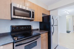 Kitchen featuring wood-finish cabinetry, dark countertops, and stainless steel appliances including a microwave, electric range, and refrigerator - 