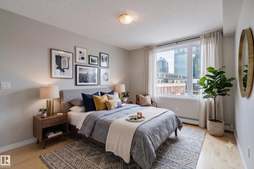 Bedroom featuring wood-finish flooring and a large window with city architecture visible - 608 10303 105 Street, Edmonton, AB 
