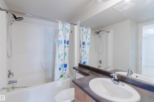 Bathroom featuring a white bathtub and shower combination with a curved shower curtain rod, a single vanity with an integrated sink, a dark countertop, and a large wall-mounted mirror - 608 10303 105 Street, Edmonton, AB 