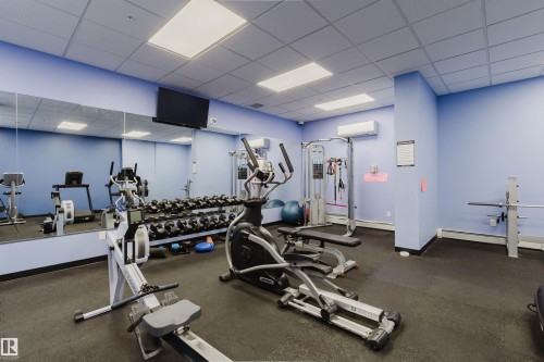 Fitness center featuring rubber flooring, mirrored wall, recessed lighting, wall-mounted television, and a variety of exercise equipment - 608 10303 105 Street, Edmonton, AB 