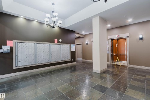 Building lobby featuring multi-tone slate tile flooring, a dark bronze mail center, a chandelier, recessed ceiling lighting, and an elevator with wood-finish interior panels - 608 10303 105 Street, Edmonton, AB 