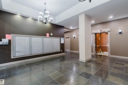 Building lobby featuring multi-tone slate tile flooring, a dark bronze mail center, a chandelier, recessed ceiling lighting, and an elevator with wood-finish interior panels - 