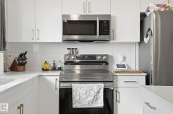 Kitchen featuring white cabinetry with gold-finish hardware, stainless steel appliances, a white tile backsplash, and light-toned countertops - 