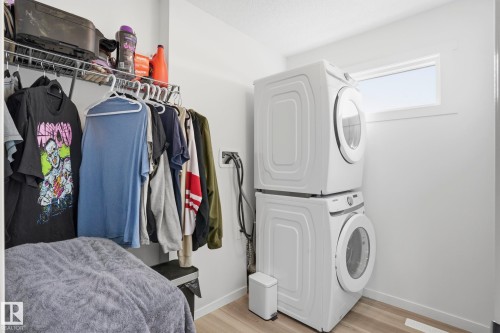 Dedicated laundry area featuring a stacked washer and dryer, wood-finish flooring, and a high window - 58 Jensen Gate, St. Albert, AB 