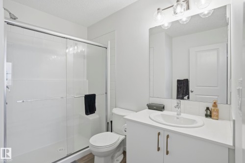 Full bathroom featuring a walk-in shower with clear glass doors, a white vanity with a single basin sink, and a large wall-mounted mirror with overhead lighting - 58 Jensen Gate, St. Albert, AB 