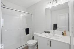 Full bathroom featuring a walk-in shower with clear glass doors, a white vanity with a single basin sink, and a large wall-mounted mirror with overhead lighting - 
