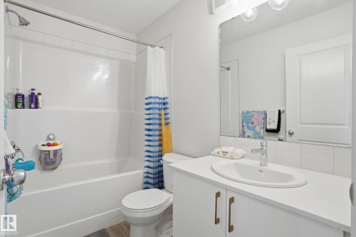 Full bathroom featuring a white tub with shower, white tile surround, and a vanity with a drop-in sink - 58 Jensen Gate, St. Albert, AB 