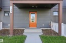 Modern facade featuring horizontal dark grey siding and a prominent orange entry door with a glass insert - 58 Jensen Gate, St. Albert, AB 