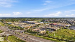 Expansive aerial showcasing a commercial district with multiple retail establishments, extensive paved parking areas, and mature landscaping - 