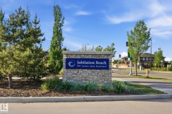 Stone entry monument with a blue placque featuring "Jubilation Beach" and "205 Jensen Lakes Boulevard." The monument is surrounded by manicured landscaping including evergreen trees and ornamental grasses - 