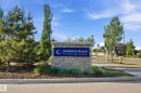 Stone entry monument with a blue placque featuring "Jubilation Beach" and "205 Jensen Lakes Boulevard." The monument is surrounded by manicured landscaping including evergreen trees and ornamental grasses - 58 Jensen Gate, St. Albert, AB 