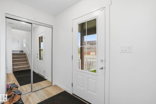 Entryway featuring wood-finish flooring, a white paneled door with glass inserts, and a sliding mirrored closet door - 58 Jensen Gate, St. Albert, AB 