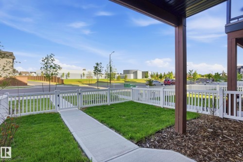 Fenced front yard featuring a concrete pathway, green lawn, and a white picket fence with a gate - 58 Jensen Gate, St. Albert, AB 