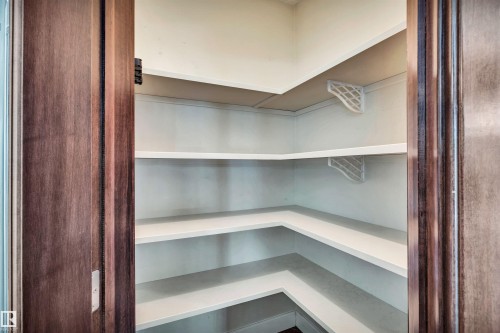 Spacious walk-in pantry featuring multiple white built-in shelves and a rich wood-finish door frame - 9 Shorewood Crescent, Leduc, AB - Indoor With Storage