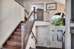 Two-story foyer featuring a grand staircase with dark wood-finish treads and white balusters - 
