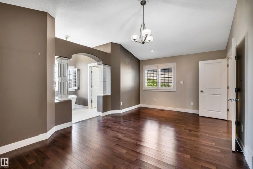 Hardwood-finish flooring throughout, complemented by a contemporary chandelier, a window with louvered shutters, and an arched entry - 9 Shorewood Crescent, Leduc, AB - Indoor Photo Showing Other Room