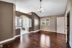 Hardwood-finish flooring throughout, complemented by a contemporary chandelier, a window with louvered shutters, and an arched entry - 