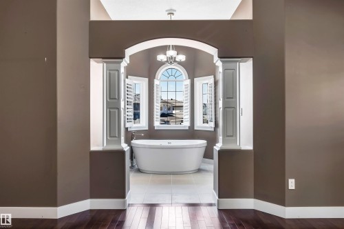 Freestanding soaking tub with a floor-mounted faucet, arched window, and white plantation shutters, set within an arched entryway with decorative columns - 9 Shorewood Crescent, Leduc, AB - Indoor Photo Showing Bathroom