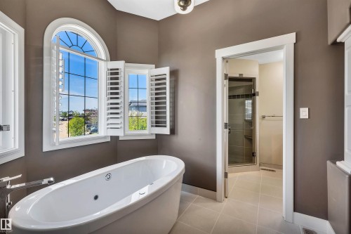 Freestanding bathtub with integrated jets, complemented by an arched window with white plantation shutters - 9 Shorewood Crescent, Leduc, AB - Indoor Photo Showing Bathroom