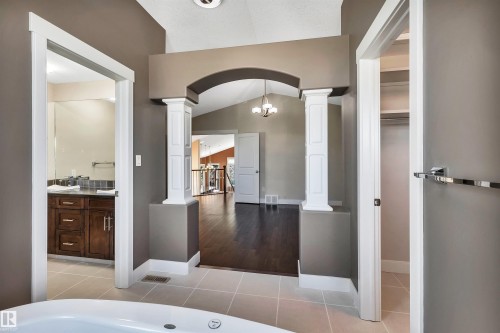 Soaking tub with tile surround, arched entryway with decorative columns, wood-finish flooring, vaulted ceiling, and recessed lighting - 9 Shorewood Crescent, Leduc, AB - Indoor Photo Showing Bathroom
