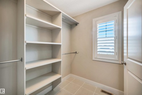 Walk-in closet featuring built-in shelving, hanging rods, light-toned wall paint, ceramic tile flooring, and a window with white louvered shutters - 9 Shorewood Crescent, Leduc, AB - Indoor With Storage