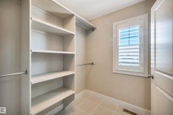Walk-in closet featuring built-in shelving, hanging rods, light-toned wall paint, ceramic tile flooring, and a window with white louvered shutters - 