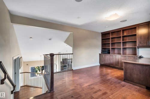 Open-concept loft space featuring rich wood-finish flooring, recessed lighting, and a comprehensive built-in shelving unit with lower cabinetry - 9 Shorewood Crescent, Leduc, AB - Indoor