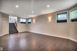 Spacious room featuring large format tile flooring, recessed ceiling lighting, three windows with blinds, two wall sconces, and a staircase with a wood handrail - 