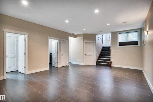 Spacious lower level featuring large format tile flooring, recessed lighting, and a staircase with dark treads and white risers - 9 Shorewood Crescent, Leduc, AB - Indoor Photo Showing Other Room