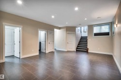Spacious lower level featuring large format tile flooring, recessed lighting, and a staircase with dark treads and white risers - 