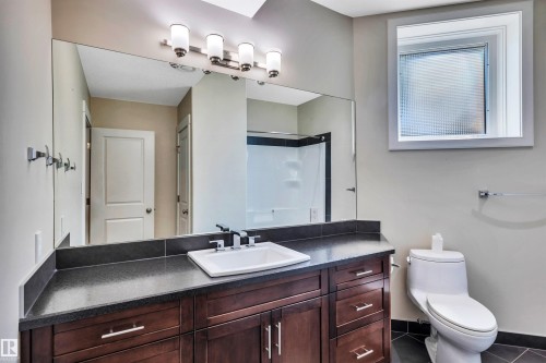 Bathroom featuring a rich wood-finish vanity with a dark countertop, white undermount sink, and chrome fixtures - 9 Shorewood Crescent, Leduc, AB - Indoor Photo Showing Bathroom