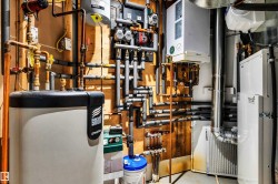 Utility area featuring a water heater, complex piping, a wall-mounted boiler system, and an air exchange unit - 