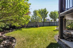 Expansive green lawn surrounded by mature trees, privacy fencing, and decorative rock landscaping - 