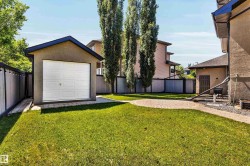 Expansive grassy yard featuring a detached single-car garage, perimeter fencing, and a circular paver patio - 