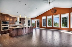 Spacious open-concept room featuring a complete kitchen with a large island, stainless steel appliances, and dark wood cabinetry - 