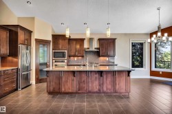 Gourmet kitchen featuring rich wood cabinetry, stainless steel appliances, a spacious island with a stone countertop, and a mosaic tile backsplash - 