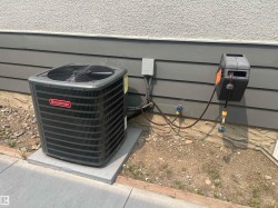 Exterior mechanical systems featuring a Goodman air conditioning unit on a concrete pad, wall-mounted hose reel, and exterior electrical conduit - 