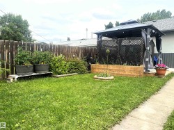 Expansive backyard featuring a permanent gazebo structure, raised garden beds, established garden plantings, a wood fence, and a concrete pathway - 