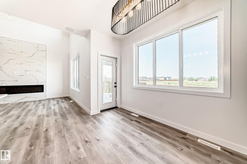 Spacious interior featuring wood-finish flooring, a contemporary linear fireplace with a marble-look surround, and ample natural light from large windows - 14 Tenuto Link, Spruce Grove, AB - Indoor Photo Showing Other Room