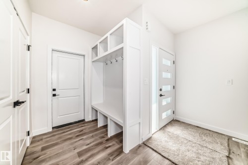 Entryway featuring a built-in mudroom bench with cubbies and hooks, wood-finish flooring, two panel interior doors with matte black hardware, and a modern front door with frosted glass inserts - 14 Tenuto Link, Spruce Grove, AB - Indoor Photo Showing Other Room
