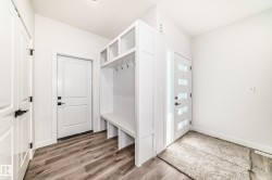 Entryway featuring a built-in mudroom bench with cubbies and hooks, wood-finish flooring, two panel interior doors with matte black hardware, and a modern front door with frosted glass inserts - 