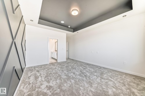 Spacious room featuring a textured accent wall, recessed ceiling with contrasting paint, and gray patterned carpeting - 14 Tenuto Link, Spruce Grove, AB - Indoor Photo Showing Other Room