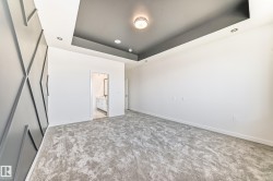 Spacious room featuring a textured accent wall, recessed ceiling with contrasting paint, and gray patterned carpeting - 