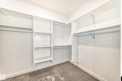 Walk-in closet featuring white built-in shelving, multiple hanging rods, and gray textured carpeting - 
