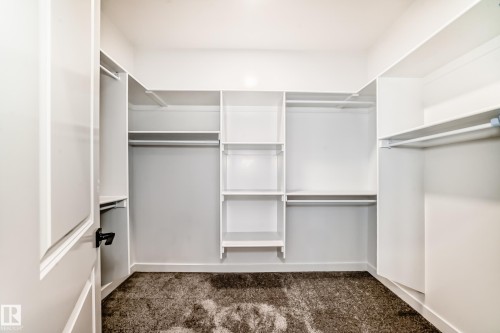 Walk-in closet featuring built-in shelving, multiple hanging rods, white trim, and dark textured carpeting - 14 Tenuto Link, Spruce Grove, AB - Indoor With Storage