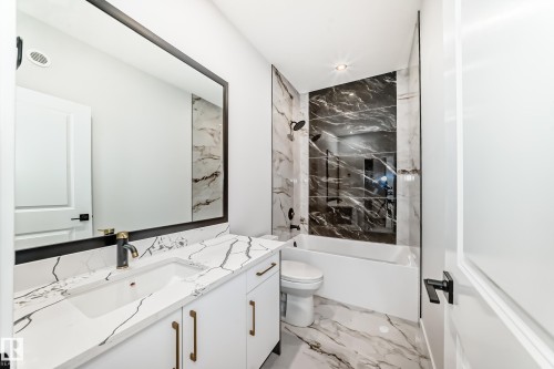 Bathroom featuring a vanity with a white countertop and integrated sink, a large framed mirror, a dark tiled accent wall in the shower, a white bathtub, and patterned tile flooring - 14 Tenuto Link, Spruce Grove, AB - Indoor Photo Showing Bathroom