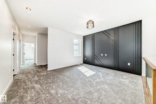 Spacious room featuring a dark accent wall with geometric paneling, gray textured carpeting, and a contemporary ceiling light fixture - 14 Tenuto Link, Spruce Grove, AB - Indoor Photo Showing Other Room