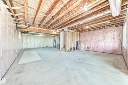 Unfinished basement featuring exposed wood joists, concrete flooring, insulated walls, and visible utility infrastructure - 