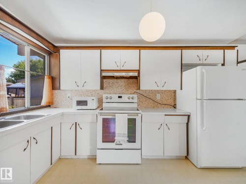 Kitchen featuring white cabinetry, a dual basin stainless steel sink, and a mosaic tile backsplash - 15011 72A Street, Edmonton, AB 